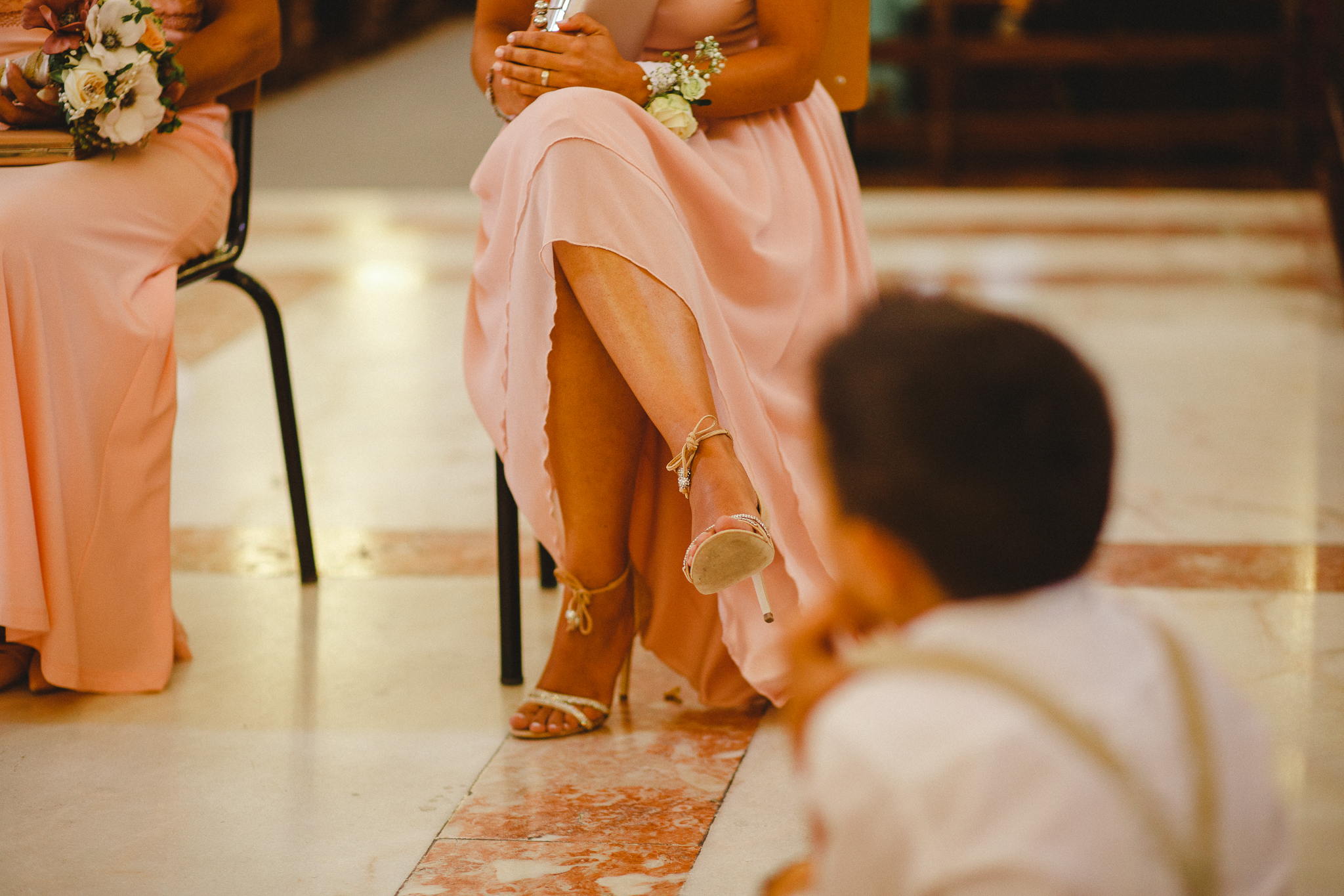 Wedding guest sitting in church in light pink dress and elegant high heels.