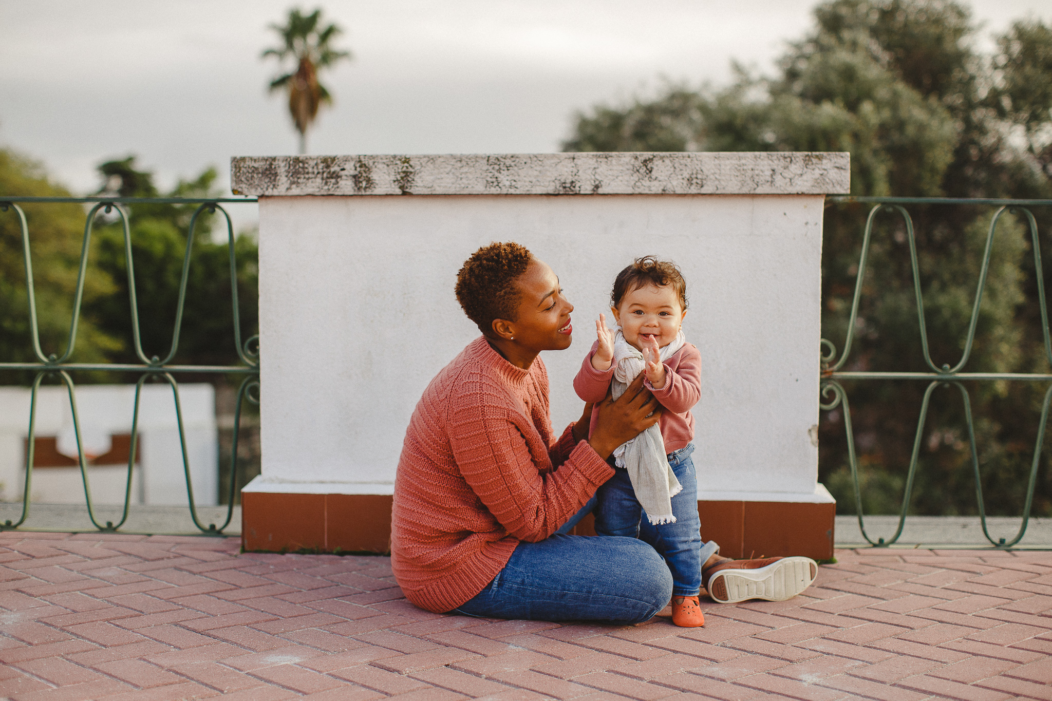 Mom sitting on the ground with baby daughter clapping, during a family photo shoot in Lisbon with Hello Twiggs.