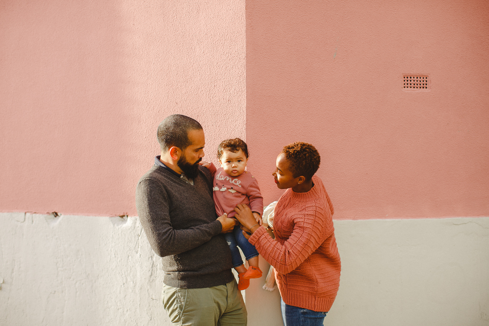 Family of three on a pink corner in Lisbon during a family photo shoot with photographer Hello Twiggs.