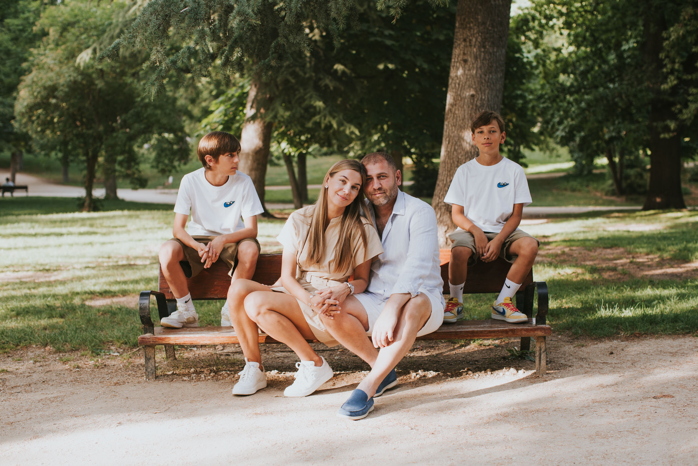 Family poses in a relaxed way on a bench at El Retiro, Madrid, during a family photo session.